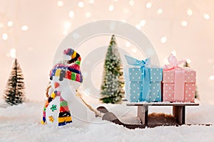 Toy snowman pulling small wooden sleigh with a Christmas gifts.