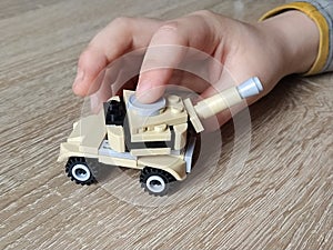 Toy tank on a wooden table. Plastic toy. Craft from a children`s designer. The beige color of the tank, defocused image. Baby