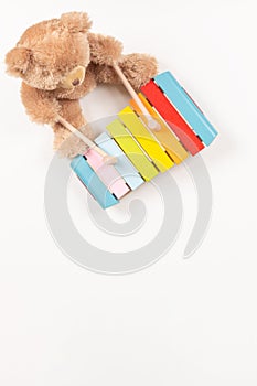Toy teddy bear playing on colorful xylophone. Kid toys on white background. Early childhood music education. Top view