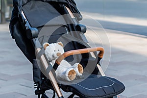 Toy teddy bear sitting in a baby stroller on blurred background of city street