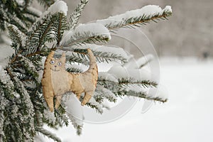 Toy tiger, cat, symbol of the eastern horoscope 2022, against the background of a snowy Christmas tree. Snowing. Blurred winter