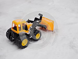 Toy tractor removes snow with a bucket in winter