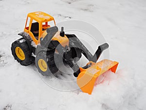 Toy tractor removes snow with a bucket in winter