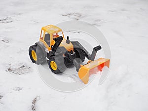 Toy tractor removes snow with a bucket in winter