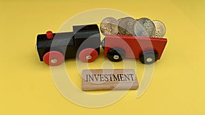 Toy train carry gold coins with investment word on wooden block. Investment and business concept.
