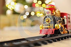 Toy train and railway on floor against Christmas lights. Space for text