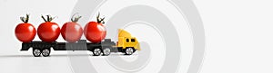 Toy truck carries fresh red tomatoes. White background. Concept for the delivery of oversized items and fresh vegetables from the