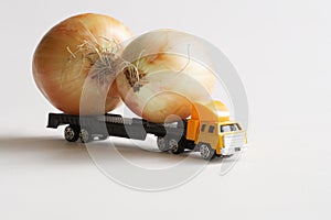 A toy truck is carrying large onion bulbs for sale. White background. Concept for the delivery of oversized items and fresh