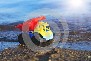Toy truck on the gold sandy beach. Red, blue and yellow car on t