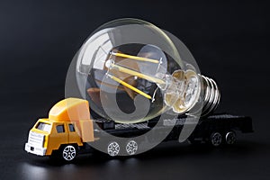 Toy truck with trailer transporting energy-saving LED bulb. Dark background. Transport, loading and unloading services for fragile