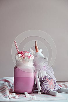 Toy unicorn with pink milk shake with cream, marshmallow and colorful decoration. Milk shake, cocktail. Unicorn coffee.