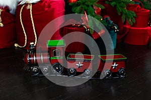 Toy vintage steam locomotive on floor under a decorated Christmas tree and gifts. Xmas toy train on Christmas tree background. Chr
