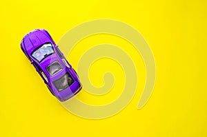 Toy violet model of car on yellow background with space for text.