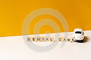 Toy white car on a yellow table from top view, the inscription of wooden blocks. The concept of a rental car and car sharing.