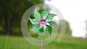 Toy windmill green pink shiny color turns in the wind on nature outdoor on a background of green grass on a Sunny summer day. Nois