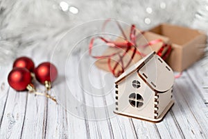 Toy wooden house on a wooden table decorated with a garland and red Christmas balls for New Year or XMAS