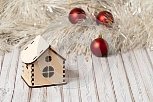 Toy wooden house on a wooden table decorated with a garland and red Christmas balls for New Year or XMAS