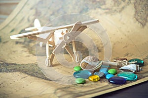 Toy wooden plane on a world map with colored stones and shells from the sea in a retro style.