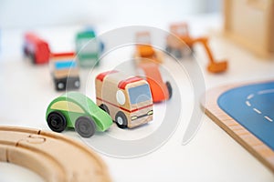 A Toy of wooden school bus drives beside a green car with many kinds of car behind