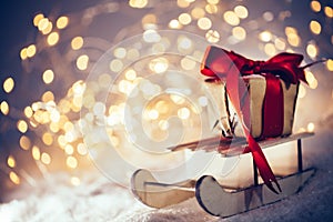 Toy wooden sledge with gift standing in snow. Christmas