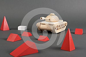Toy wooden tank and red pyramids on gray background. Politic of Militarism. Warfare concept