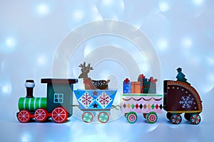 A toy wooden train carries the attributes of winter holidays on a blue abstract background. Postcard for the Christmas holidays.