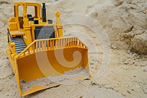 A toy yellow bulldozer digs the sand.