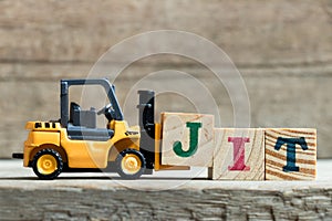 Toy yellow forklift hold letter block J to complete word JIT Abbreviation of Just in time