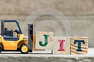 Toy yellow forklift hold letter block J to complete word JIT & x28;Abbreviation of Just in time& x29;on wood background