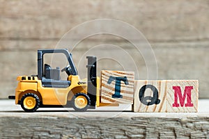 Toy yellow forklift hold letter block T to complete word T Abbreviation of total quality management