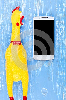 Toy yellow shrilling chicken on blue wooden background with smartphone and copy space .Template mock up for adding your design