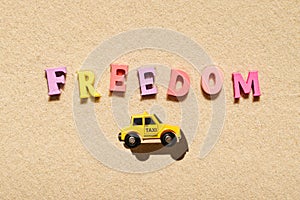 Toy yellow taxi car ride on the colorful letters of word freedom on beach sand. Concept. Fast and cheap taxi booking service.