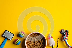 Toys for cat and bowl with dry food on yellow background. Pet care and training concept. Flat lay, top view