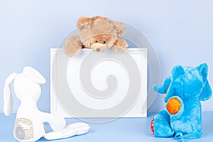 Toys with empty white frame on light blue background. Toy teddy bear and plush stuffed toys and white wooden picture