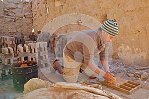 A local worker making bricks in a traditional way in a brick factory. A wooden frame is used to mold the bricks.