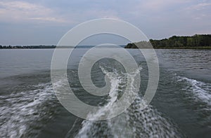 The trace on the water from the boat on the waves in the river splashes with foam