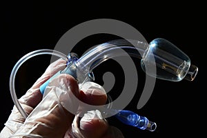 Tracheostomy cannula with inflated cuff held in doctor left hand in glove on dark background