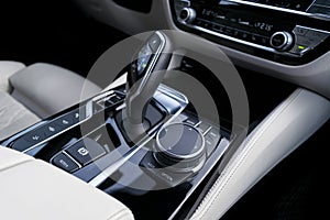 Track control buttons near automatic gear stick in a white leather interior of a modern car. Car interior details. Car inside