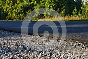 A track with fresh asphalt and a yellow dividing strip. Green grass grows on the side of the road. Summer landscape on a