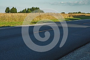 A track with fresh asphalt and a yellow dividing strip. Green grass grows on the side of the road. Summer landscape on a