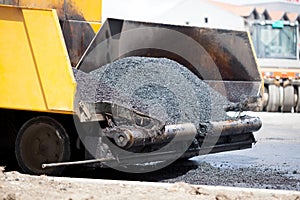 Tracked paver laying fresh asphalt pavement during road constru