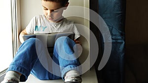 TRACKING: Cute Boy Playing The Tablet PC And Sitting On A Windowsill In The Room