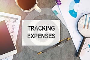 Tracking Expenses is written in a document on the office desk, smartfon and diagram