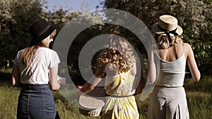 Tracking footage of three beautiful women in fancy outfit walking by the meadow or forest. Sunny day. Picnic outdoors