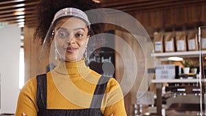 Tracking medium Close up, Female African shop owner wearing face visor standing in shop arms crossed