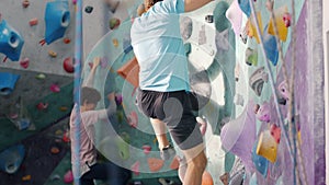 Tracking shot of adult man climbing up artificial colorful wall, woman and child in background