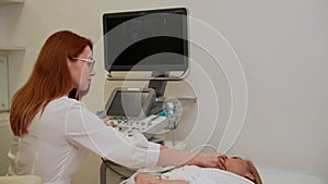 Tracking shot of checkup and scanning of thyroid gland at ultrasound scanner in hospital to young woman patient. Female