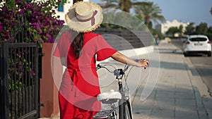 Tracking shot of confident female biker walking with bicycle in slow motion on sunny street on Cyprus. Back view