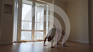 Tracking shot of flexible little kid girl doing backward bend during home workout in living room with sunny light
