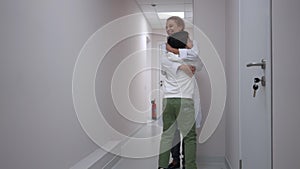 Tracking shot of joyful Caucasian boy running to doctor standing in hospital corridor hugging pediatrician. Happy